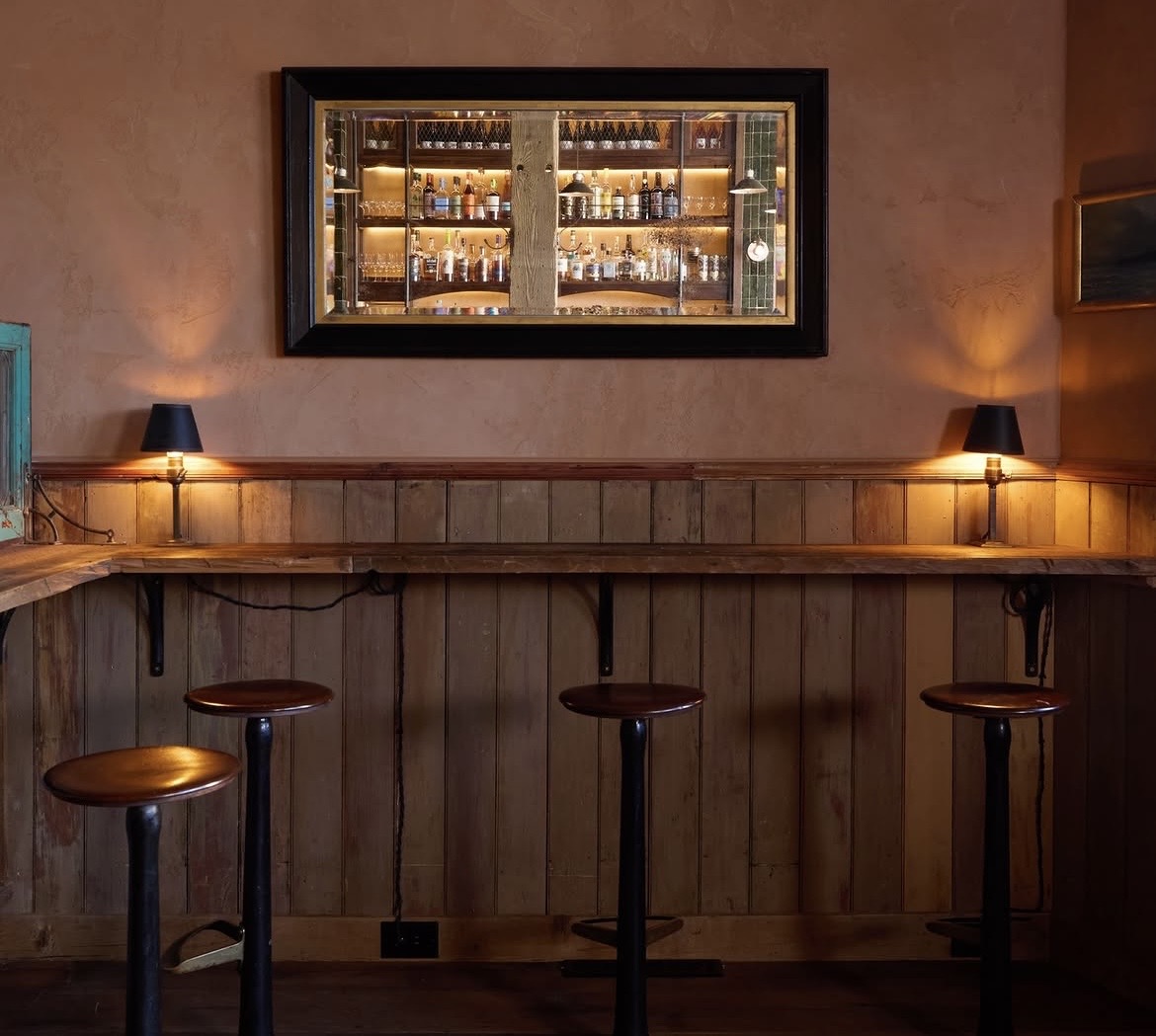 Warmly lit cocktail bar with a long counter and shelves of bottles